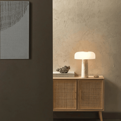 Nest table lamp on a wooden cabinet against a textured wall with abstract art.