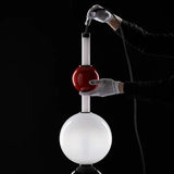 Person in white gloves pouring a red liquid from a small container into a large white sphere on a black background

