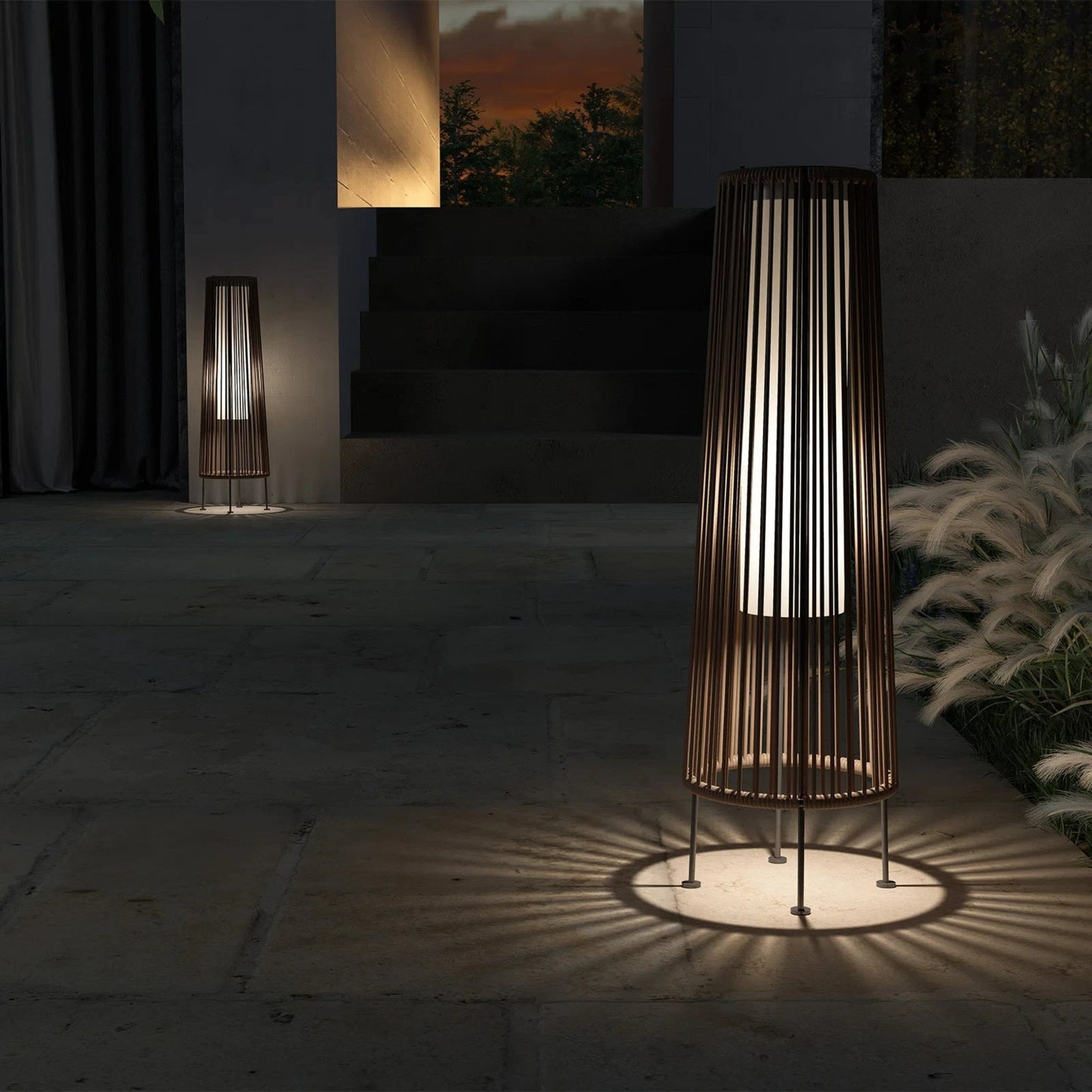 Decorative outdoor lamp casting a shadow on a stone floor with a sunset view in the background.