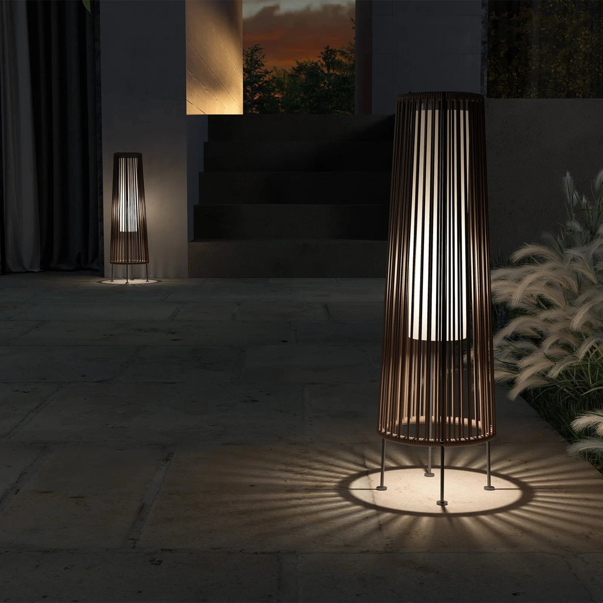 Decorative outdoor lamp casting a shadow on a stone floor with a sunset view in the background.