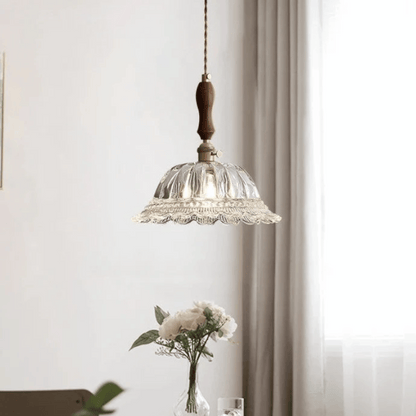 Glass pendant light fixture with wooden accent hanging above a table with flowers.