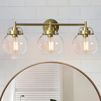 Three-light fixture with gold brackets and clear glass shades above a round mirror.