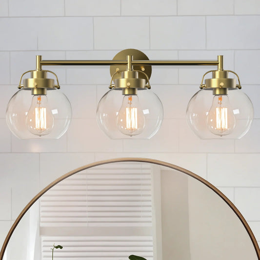 Three-light fixture with gold brackets and clear glass shades above a round mirror.