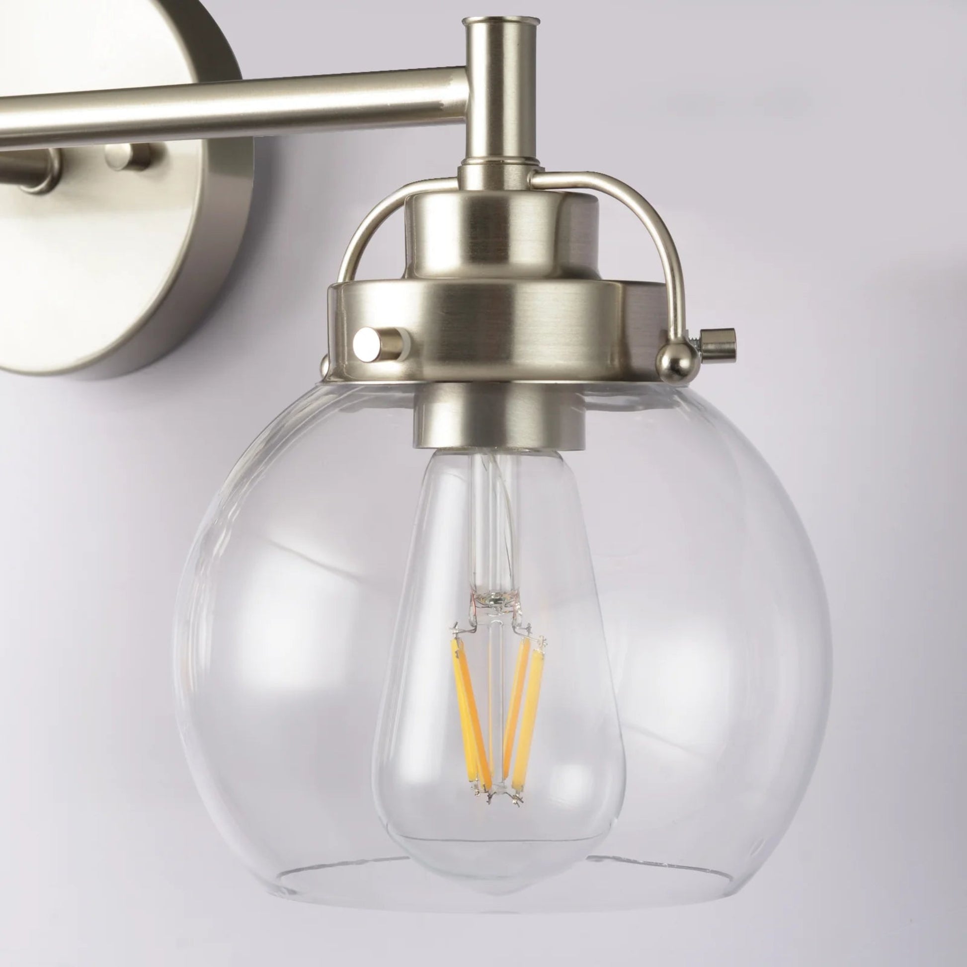 Wall-mounted light fixture with clear glass shade and metallic finish on a white background