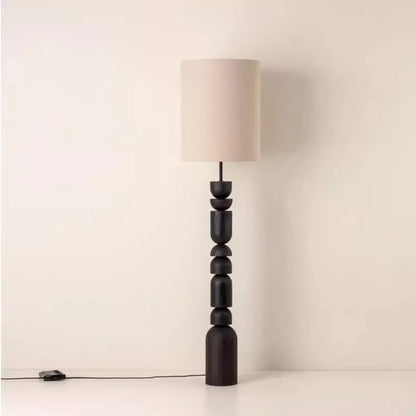 Floor lamp with a black, tiered base and a beige lampshade on a white background