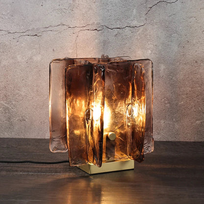 Glass table lamp with a textured design on a wooden surface and concrete wall background