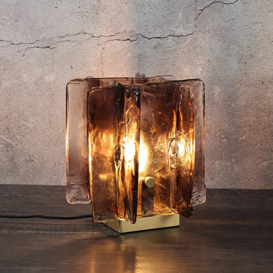 Glass table lamp with a textured design on a wooden surface and concrete wall background