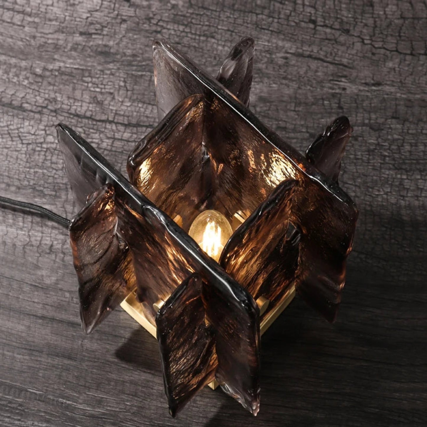 Glass table lamp with a textured design on a wooden surface and concrete wall background
