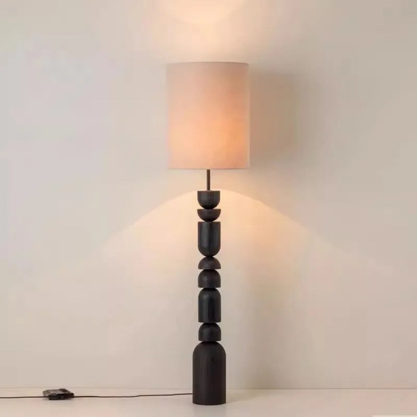 Floor lamp with a textured black base and beige shade on a plain background