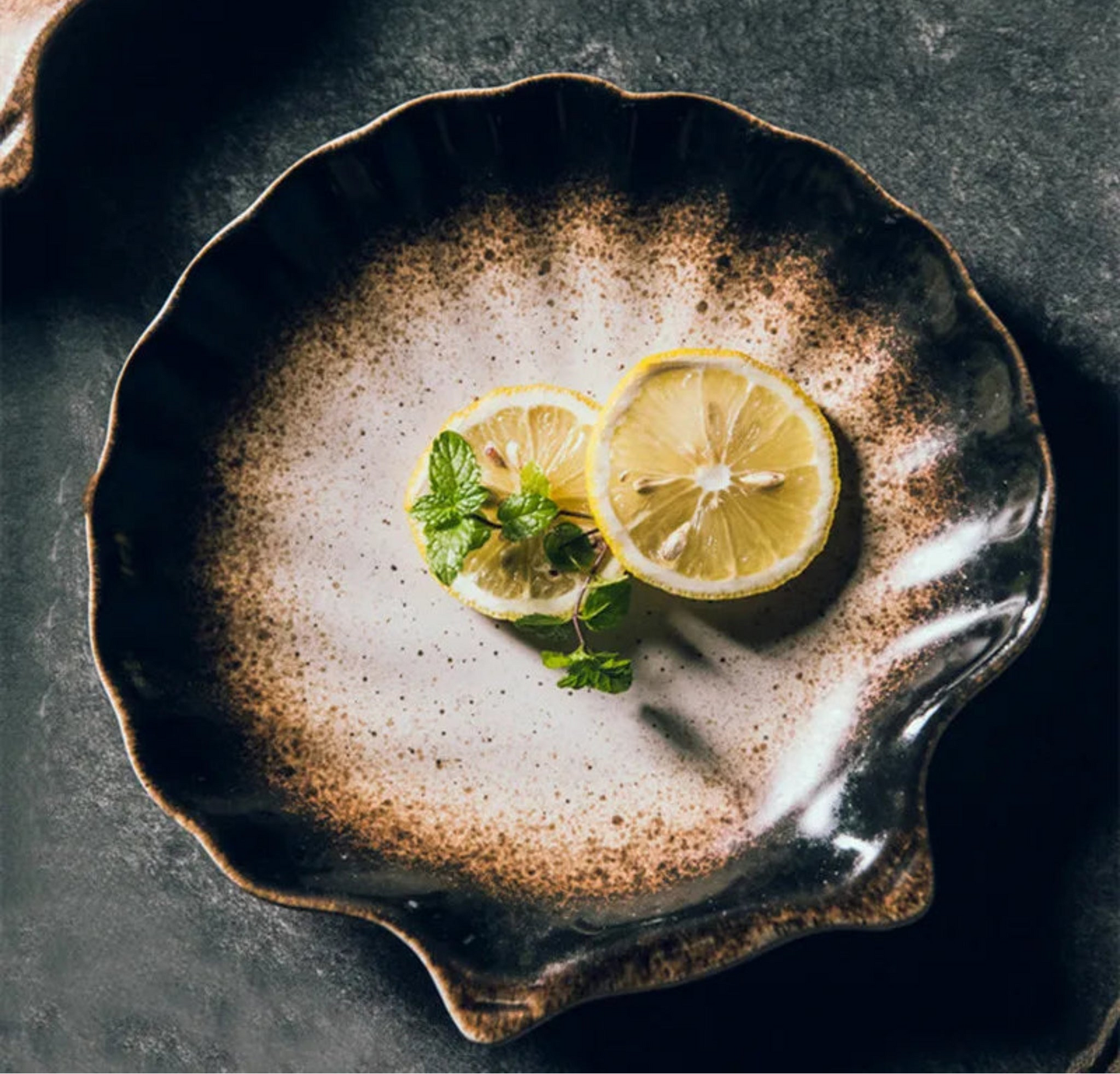 Two lemon slices with a sprig of mint on a textured ceramic plate.