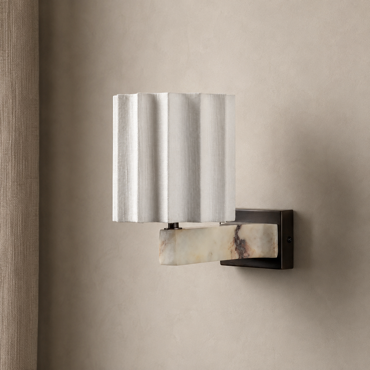 A modern wall-mounted sconce with a fluted white fabric shade and a curved cream-and-brown marble accent, attached to a dark metal bracket on a beige textured wall.
