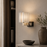 A modern wall sconce with a white pleated shade and a white-and-black marble base, mounted on a beige wall in a styled interior setting.
