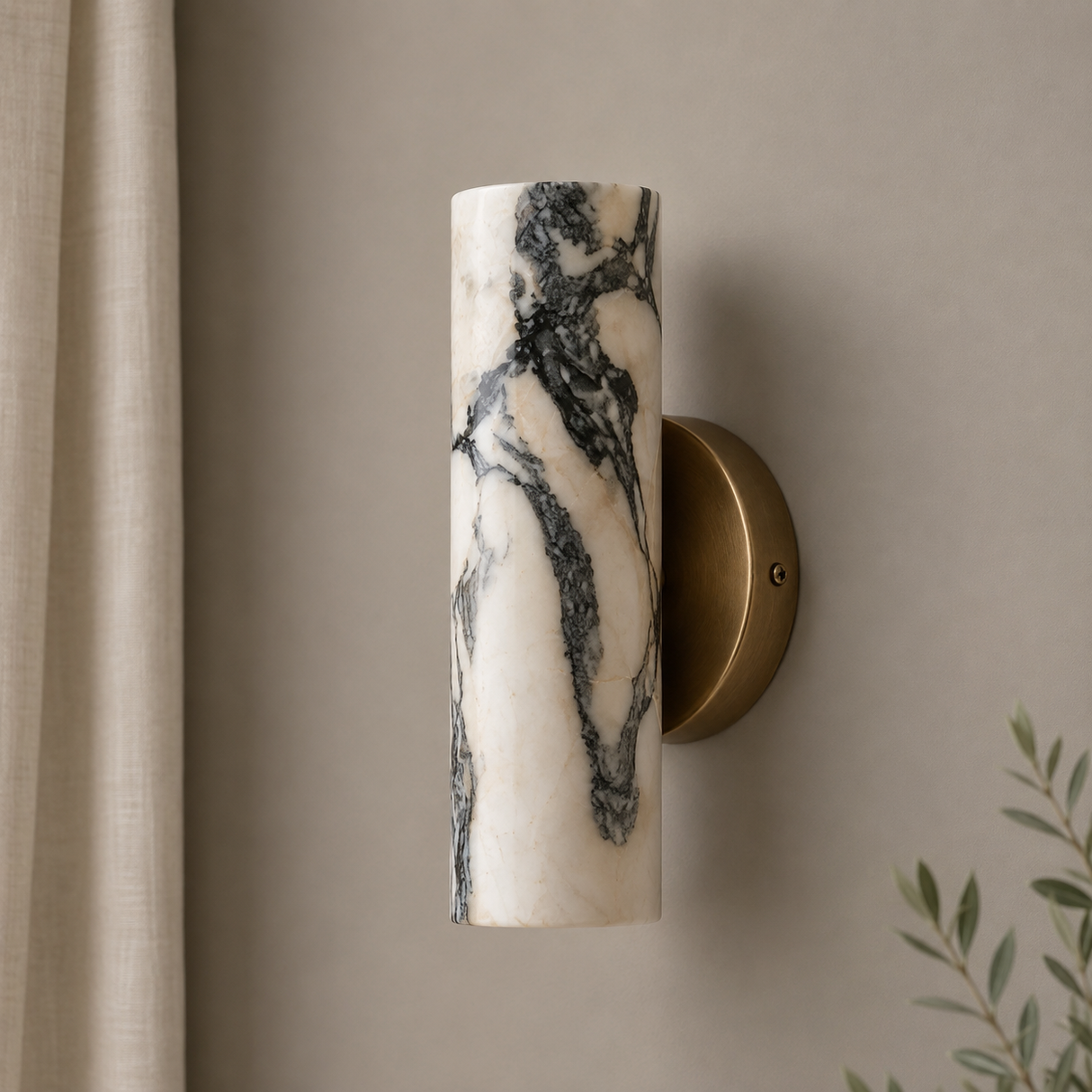 A modern wall sconce with a cylindrical marble shade featuring black and gray veining, mounted on a round brass backplate against a warm beige wall.
