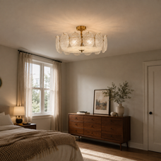 A modern semi-flush mount ceiling light fixture with a gold brass central canopy and textured, petal-like clear glass shades, shown installed in a warm, modern bedroom setting.