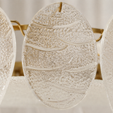 A close-up of a clear textured glass wall sconce with organic wavy patterns and a gold hanging loop, shown against a soft neutral background.
