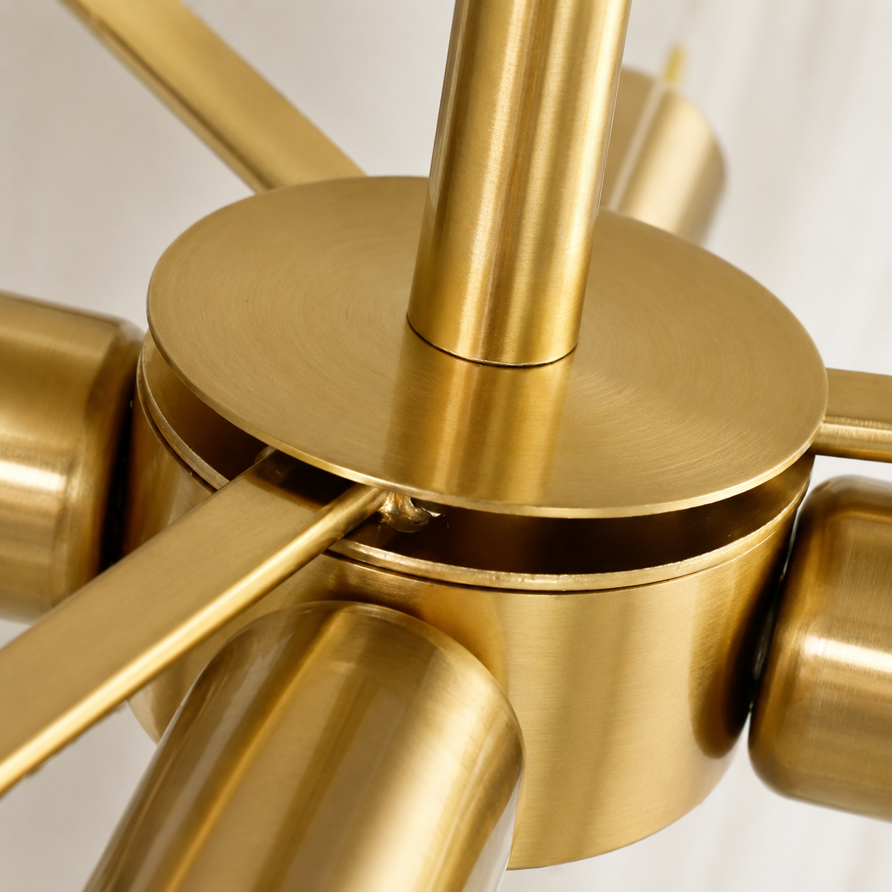 Close-up of a modern multi-arm ceiling light fixture in brushed brass/gold metal, showing the central hub and several radiating arms against a soft light background.