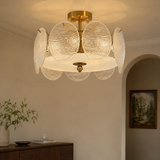 A modern semi-flush mount ceiling light fixture with multiple textured glass disc shades and a brushed brass/gold metal frame, shown installed in a warm, neutral-toned room.