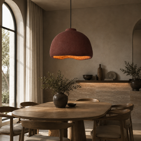A rustic terracotta-colored dome pendant light hangs over a wooden dining table in a warm, modern dining room with neutral walls and natural light from an arched window.