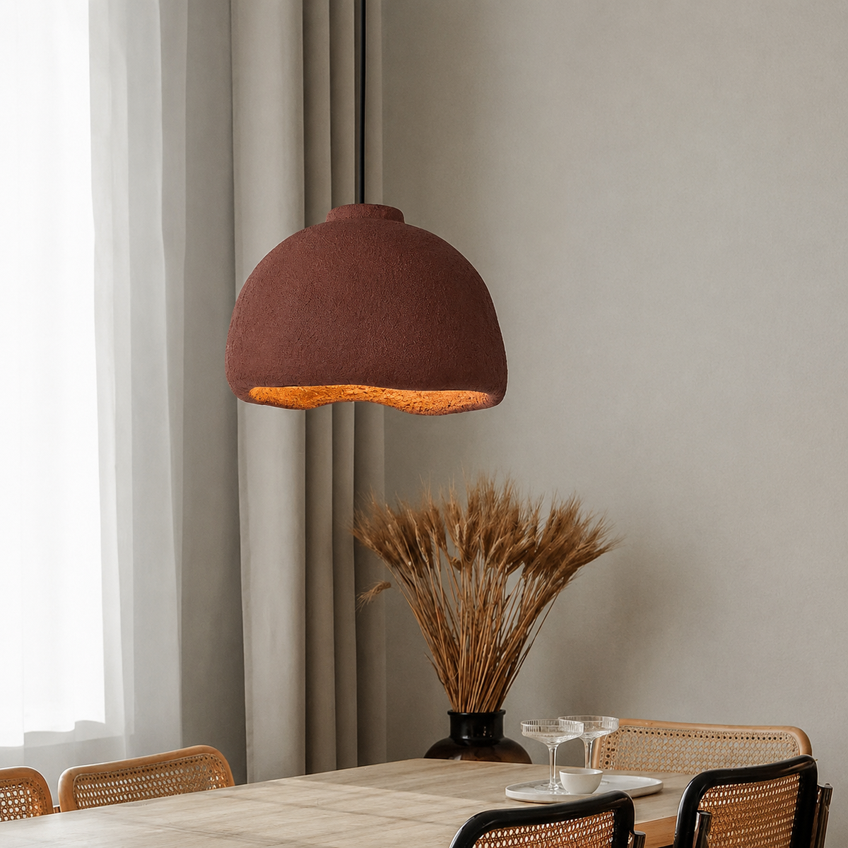 A dome-shaped pendant light with a textured rust-brown shade and a warm glowing orange interior, hanging over a dining table in a modern, neutral-toned room.