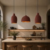 Three terracotta-colored pendant lights with a textured finish hang over a kitchen island in a warm, modern kitchen setting.