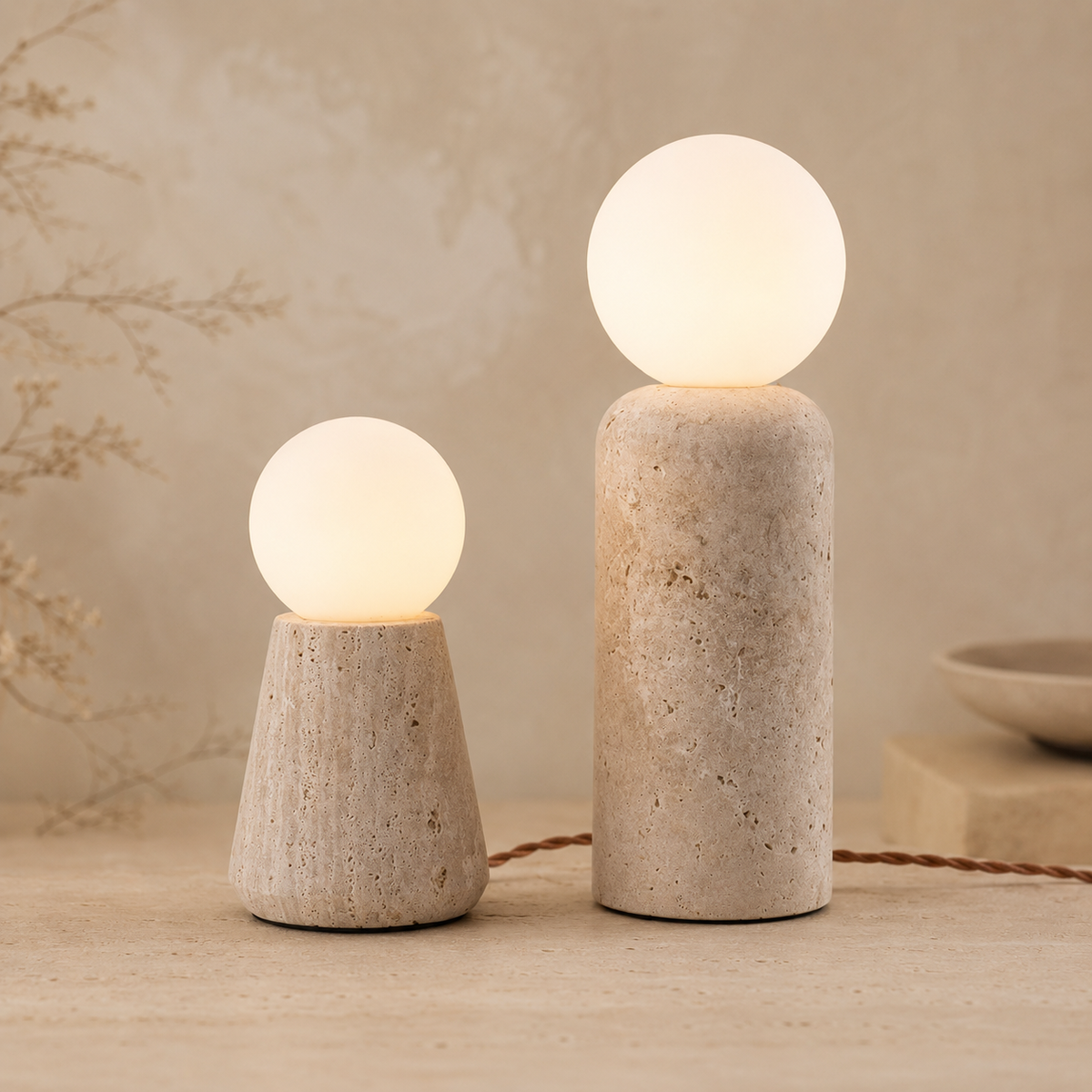 Two modern table lamps with textured stone bases and glowing frosted spherical shades, shown on a warm beige surface against a softly textured neutral background.