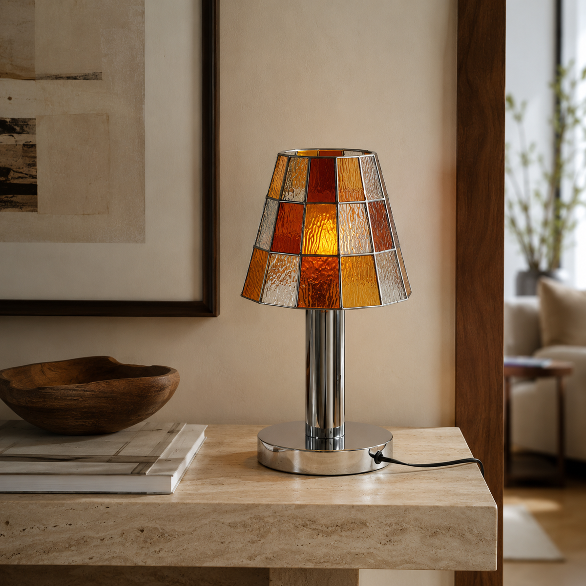 A table lamp with a stained-glass shade in amber, orange, and clear tones, set on a light stone console table in a warm, modern living room.