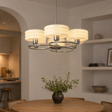 A modern 3-light chandelier with ribbed cream glass shades and a chrome ring frame, hanging over a wooden dining table in a warm, contemporary dining room.