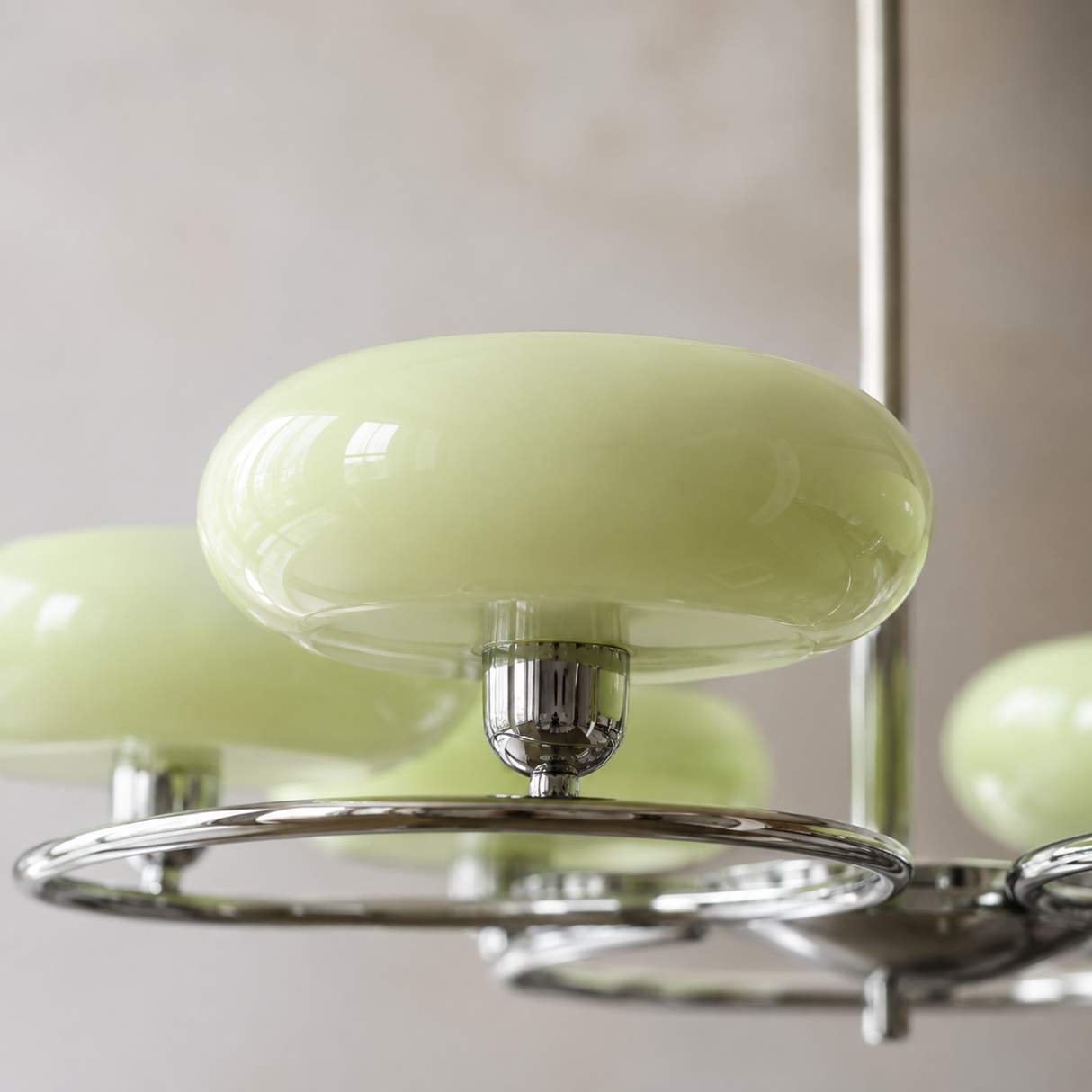 A close-up of a modern chandelier featuring glossy pale green oval glass shades suspended from a polished chrome metal frame.