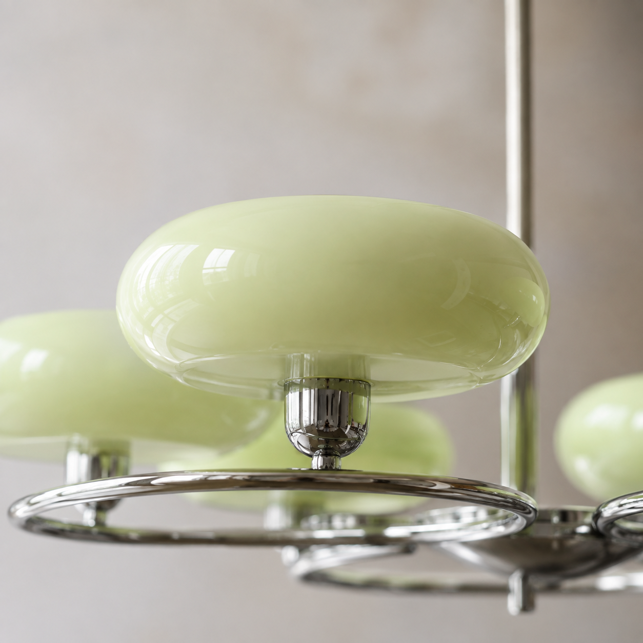 A close-up of a modern chandelier featuring glossy pale green oval glass shades suspended from a polished chrome metal frame.