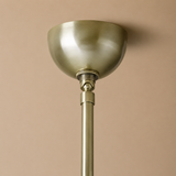 A close-up of a modern pendant light fixture with a brushed brass dome shade and matching metal stem, set against a solid warm beige background.