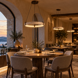 A warm, upscale restaurant interior with round wooden dining tables, upholstered chairs, hanging pendant lights, stone walls, and candlelit ambiance.