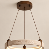 A modern pendant light fixture with a textured stone ring and a dark bronze metal frame, suspended by three cables from a matching circular ceiling canopy against a plain beige wall.