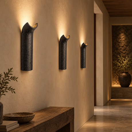 Three modern wall sconces with a textured black finish and warm gold accents, mounted on a beige wall in a styled interior hallway.