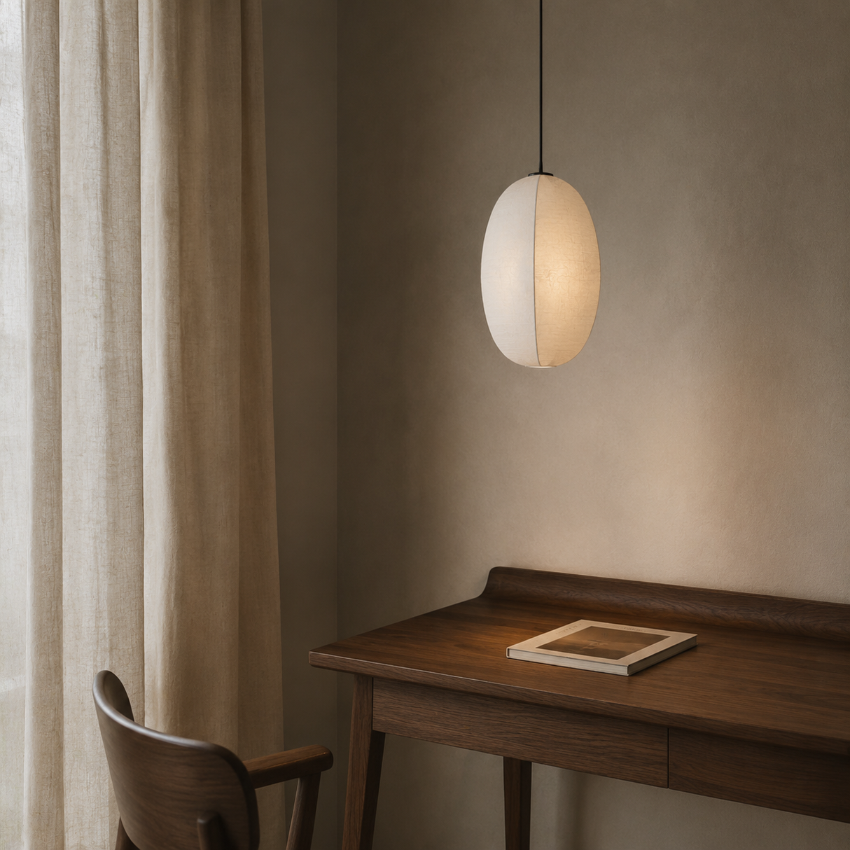 A modern oval pendant light with a warm white, semi-translucent shell hangs over a dark wood desk in a minimalist room with beige curtains and a textured wall.