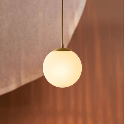 Spherical pendant light with gold fixture against a warm-toned wall.