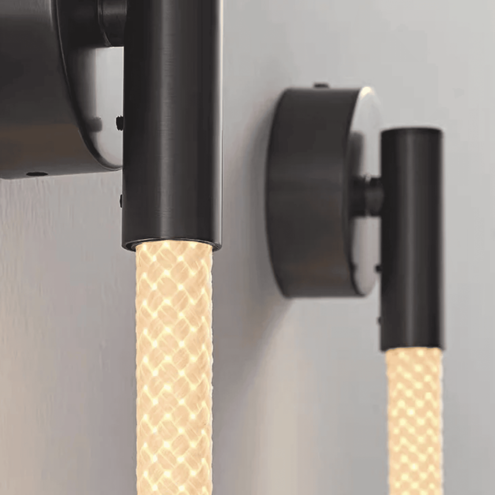 Two wall-mounted light fixtures with braided beige cables on a gray background