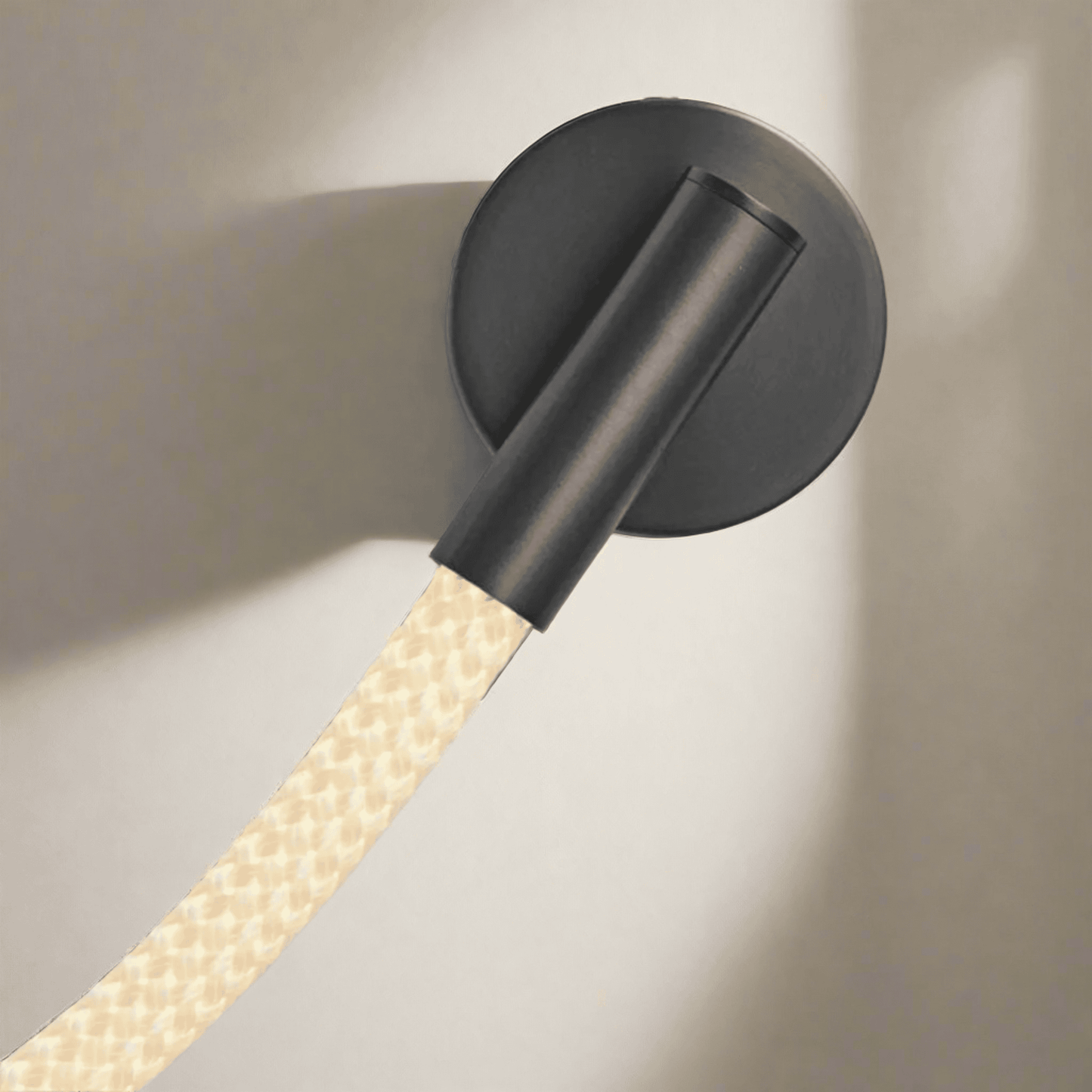 Black wall-mounted light fixture with a textured beige cable on a neutral background