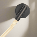 Black wall-mounted light fixture with a textured beige cable on a neutral background