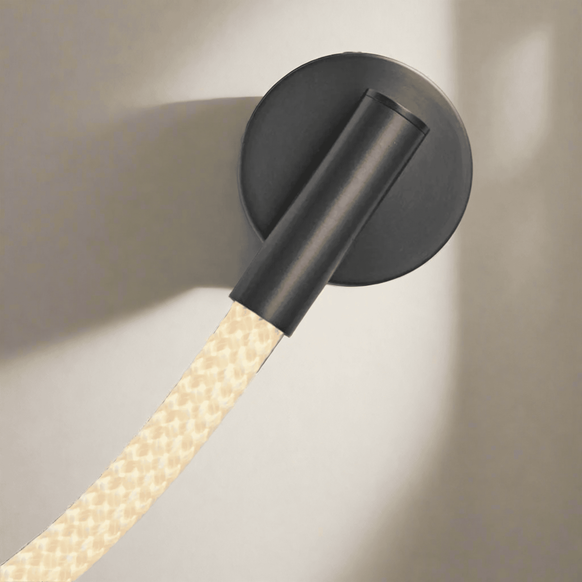 Black wall-mounted light fixture with a textured beige cable on a neutral background