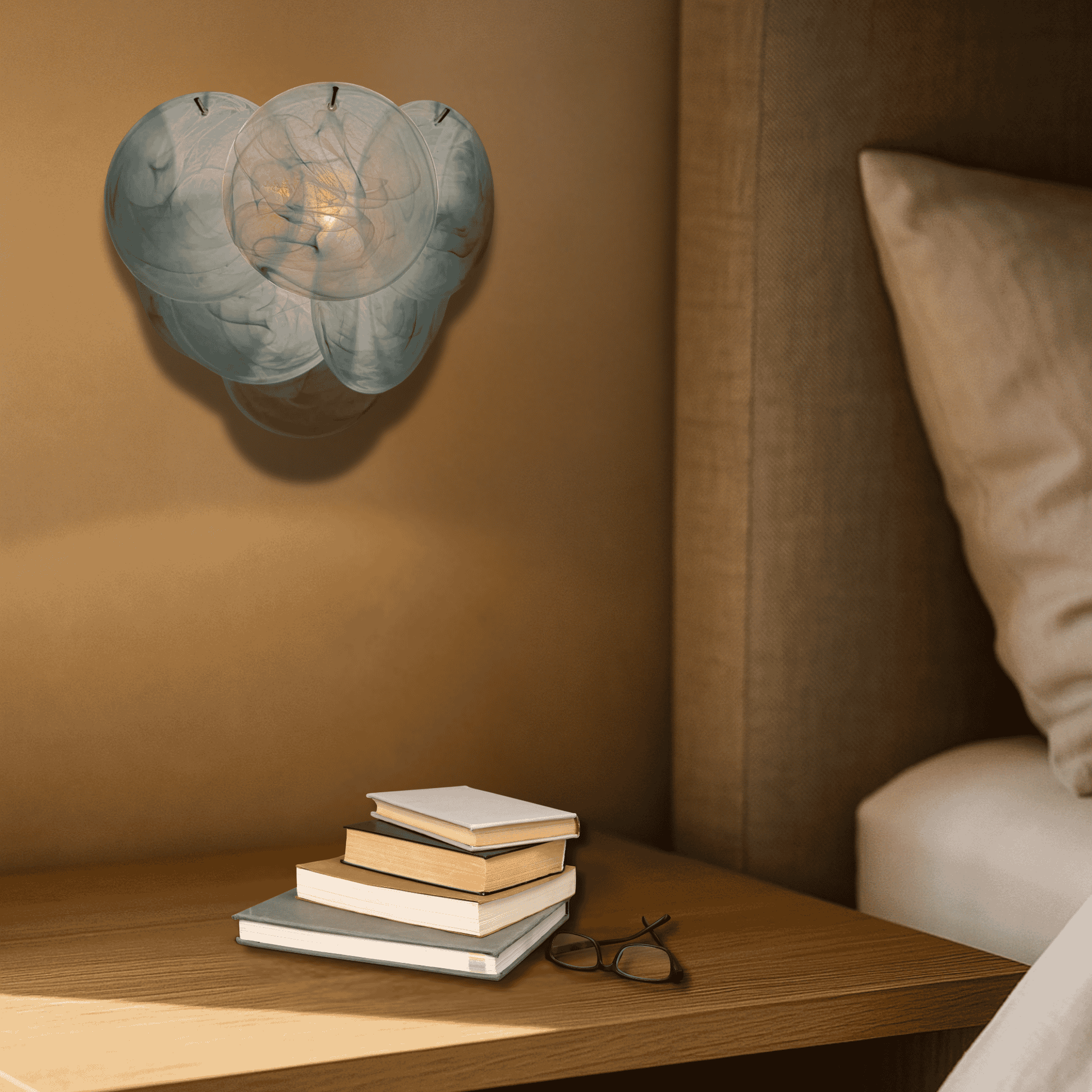 Stack of books on a wooden nightstand with a decorative wall light fixture in a bedroom setting.