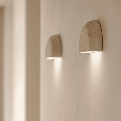 Wall-mounted natural stone sconce emitting soft light in a modern white corridor.