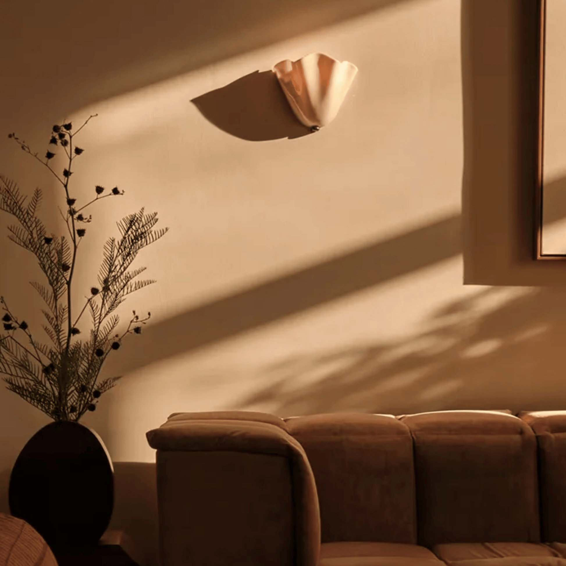 Brown sofa with a decorative plant against a beige wall with a light fixture.