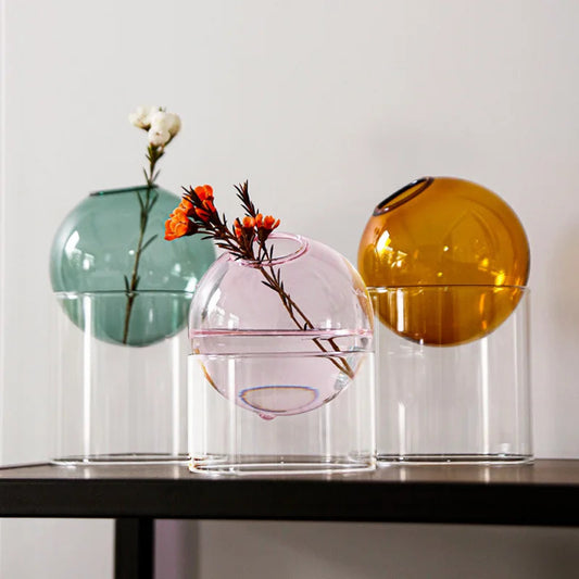 Three glass vases with floral arrangements on a table against a white wall.