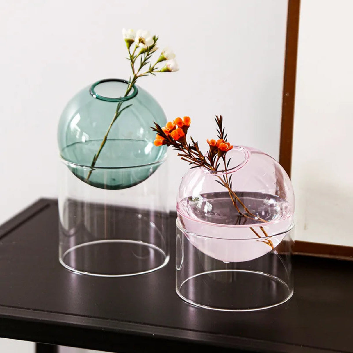 Two glass vases with floral arrangements on a dark surface.