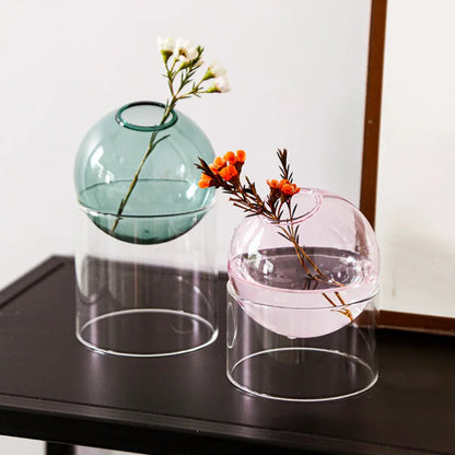 Two glass vases with floral arrangements on a dark surface.