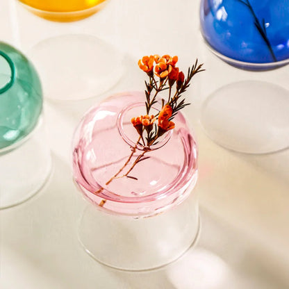 Small pink glass vase with dried flowers on a white surface