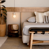 Beige sofa with decorative pillows in a living room setting with wooden furniture and plants.