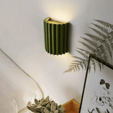 Green wall lamp on a white wall with a plant and artwork in the foreground