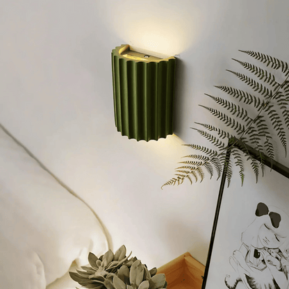 Green wall lamp on a white wall with a plant and artwork in the foreground