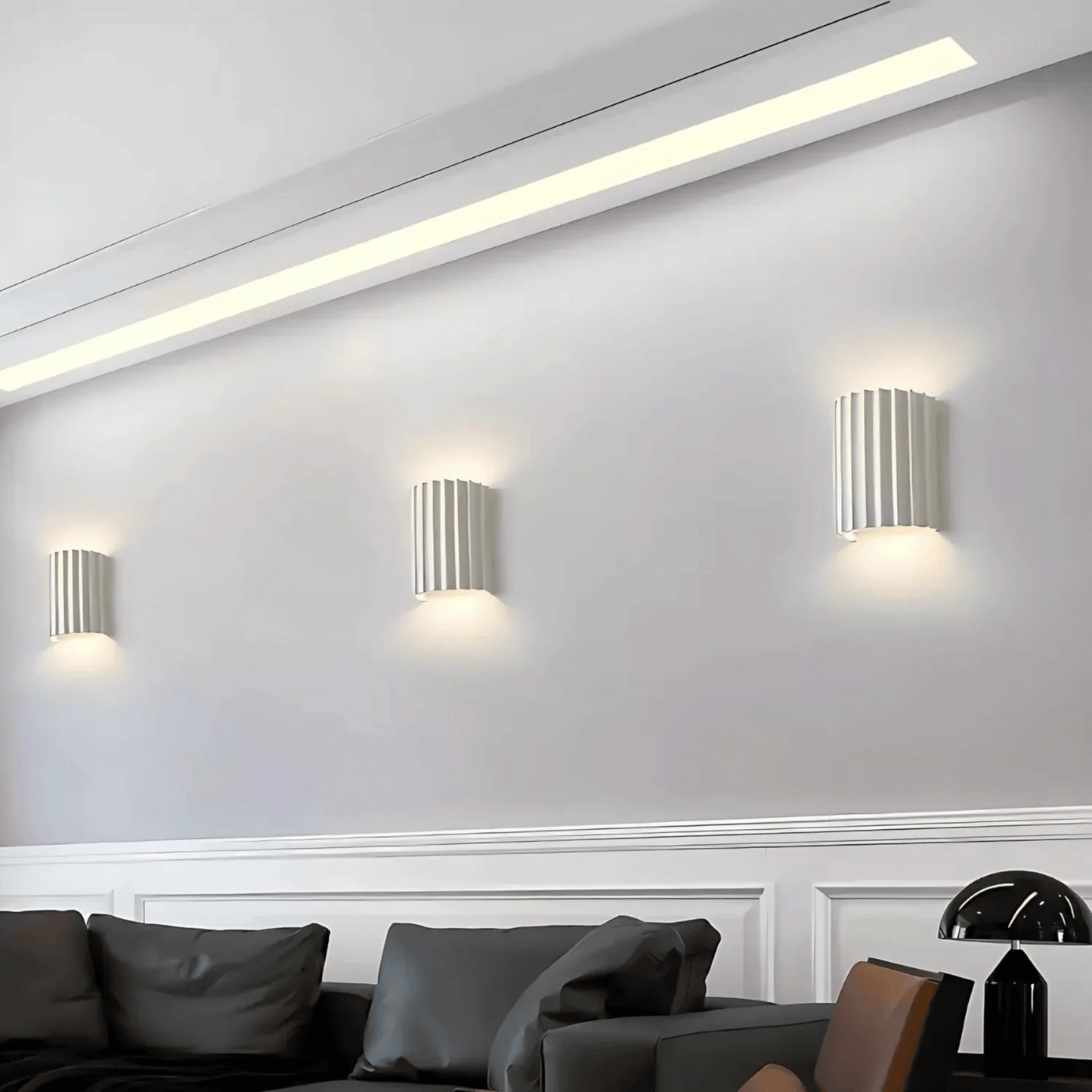Modern wall lights on a white wall with a sofa and decorative items in the foreground.